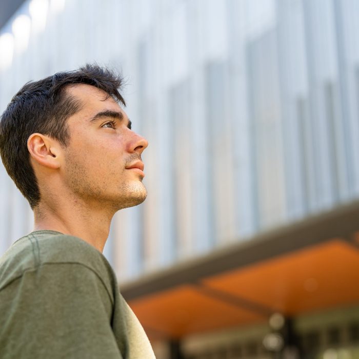 A student looking up towards the sky with the facade of a building in the background