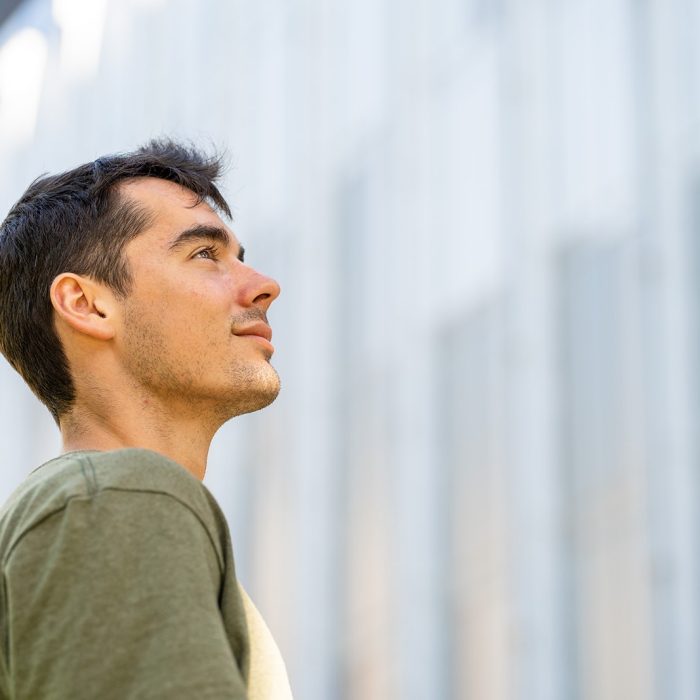 A student looking up towards the sky with the facade of a building in the background