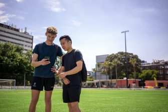 Two students looking at a mobile phone on the all-weather field at The Village Green