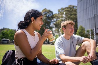 Students chatting and laughing on the grass at Alumni Park on the UNSW Kensington Campus