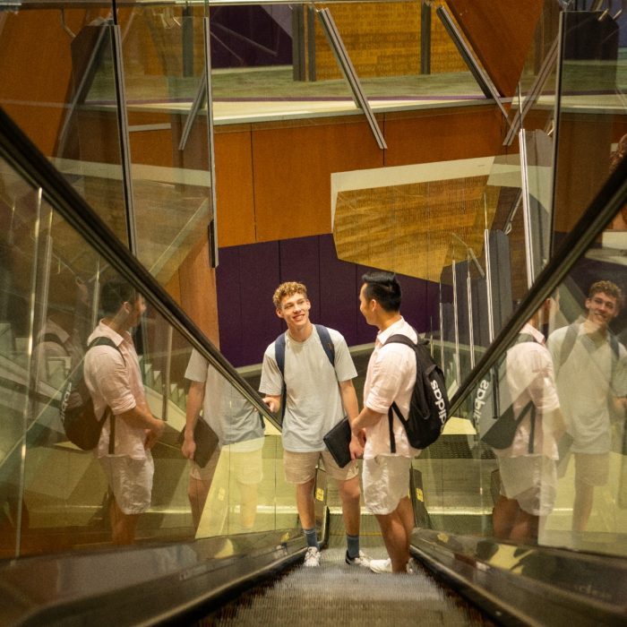 Two students using the escalator in the UNSW Law & Justice building