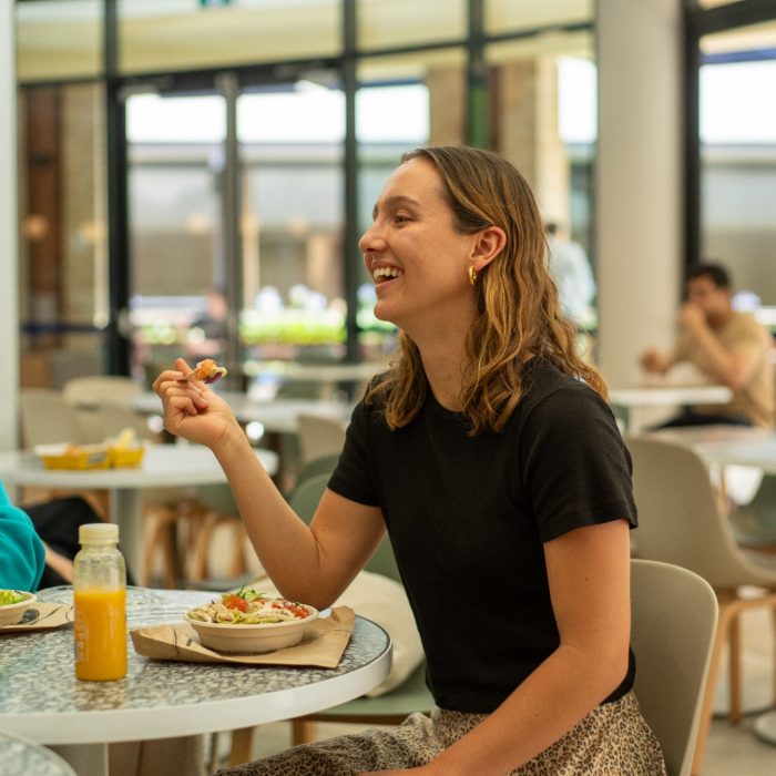 Students chatting while eating food at a table indoors on Kensington Campus