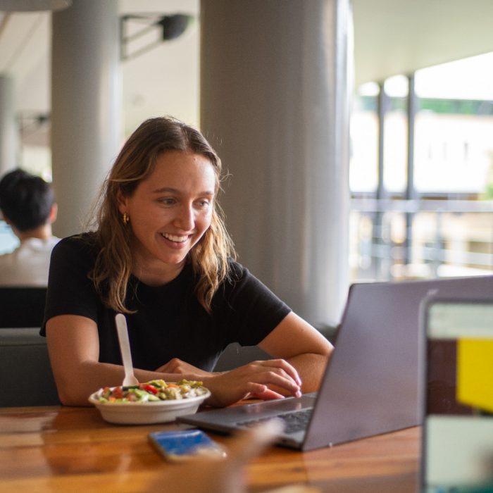 Students sitting at an outdoor table in the Quadrangle Building with their laptops