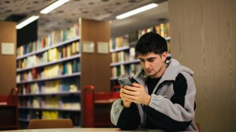 Students using their phones and laptops at a table in the library