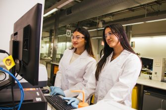 Students in a lab wearing white coats and gloves