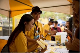 Students wearing yellow shirts speak at a market stall