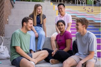 A group of five diverse students sit on stairs talking to each other