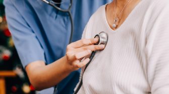 Lady coming to clinic for heart and lungs checkup, male doctor using stethoscope, listening to female patient's breath or heartbeat, sitting in clinic office