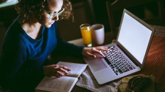 Young female student studying from a book and using laptop