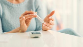 Mature woman doing blood sugar test at home in a living room. Selective focus to her finger.