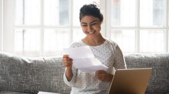 Woman sitting on couch at home reading paper notice receive good news feels happy, cheerful student female looking at document enjoy exam results or college admission letter concept