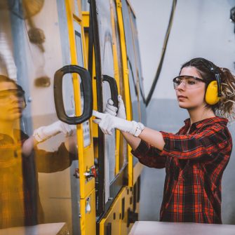 Portrait of apprentice engineering worker young woman working, examining and operating CNC plastic injection molding machinery in factory warehouse after studied manufacturing apprenticeship program certifies XXXL
