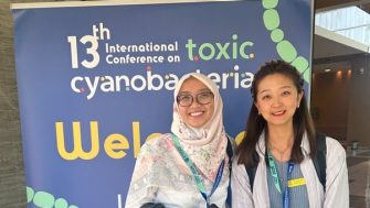 Fitri and Daisy in front of conference banner at 13th ICTC