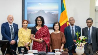 Six people pose together in a meeting room beside the Sri Lankan flag.
