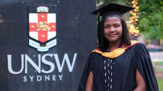graduate standing in front of unsw sign