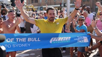 Chris Tunrbull stands with arms raised as he crosses a finishing line