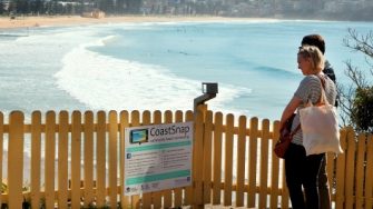 Couple looking at Coast snap sign on Manly beach