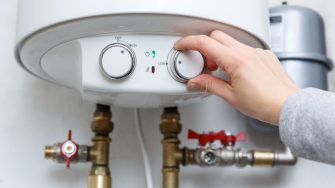 Female hand puts thermostat of electric water heater (boiler) in low low power consumption mode . Household energy saving equipment