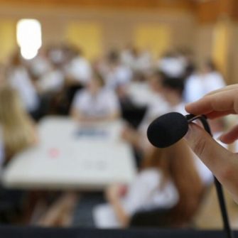 A hand holds a lectern microphone with the background blurred