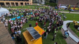 A large crowd gathers on the UNSW campus lawn around a solar-powered vehicle during a student engineering event.
