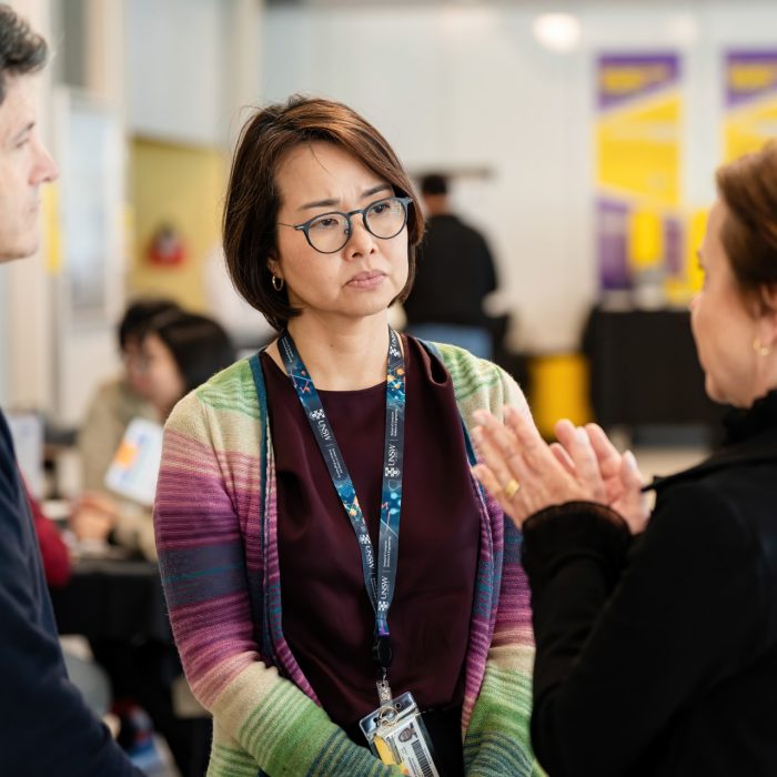 Three attendees in conversation, with one gesturing while the others listen at the UNSW–UTS TDS Student Forum.