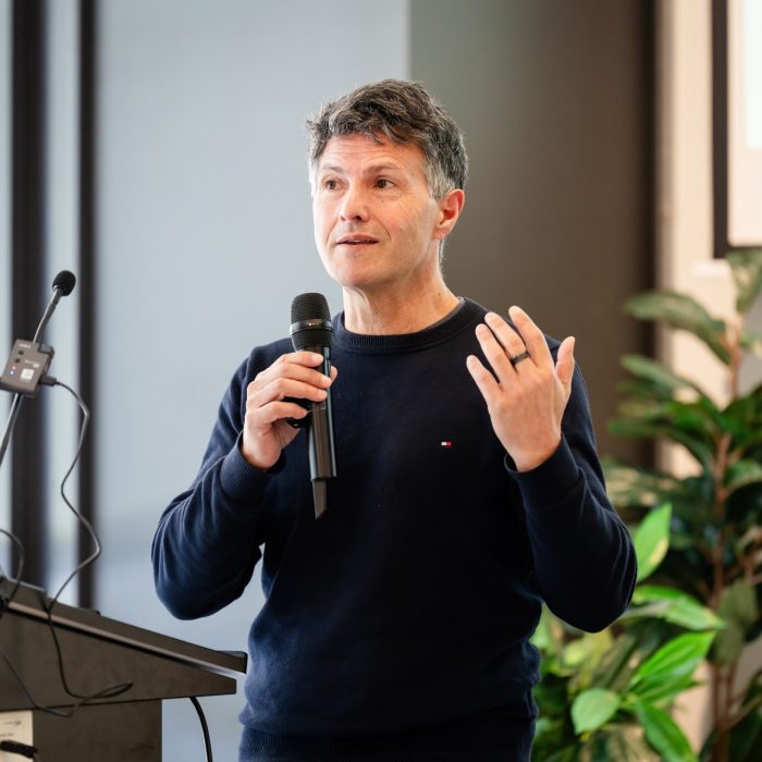 A speaker in a navy jumper holding a microphone and gesturing at the UNSW–UTS TDS Student Forum.