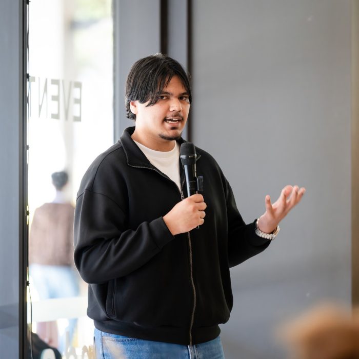 A speaker in a black jacket holding a microphone and gesturing at the UNSW–UTS TDS Student Forum.
