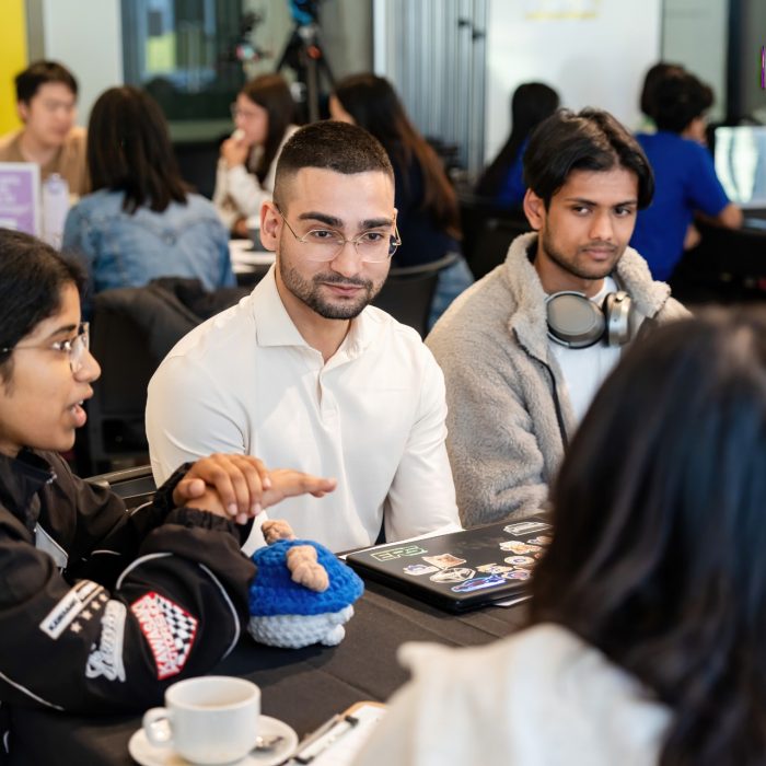 A participant gesturing during a table discussion while others listen at the UNSW–UTS TDS Student Forum.