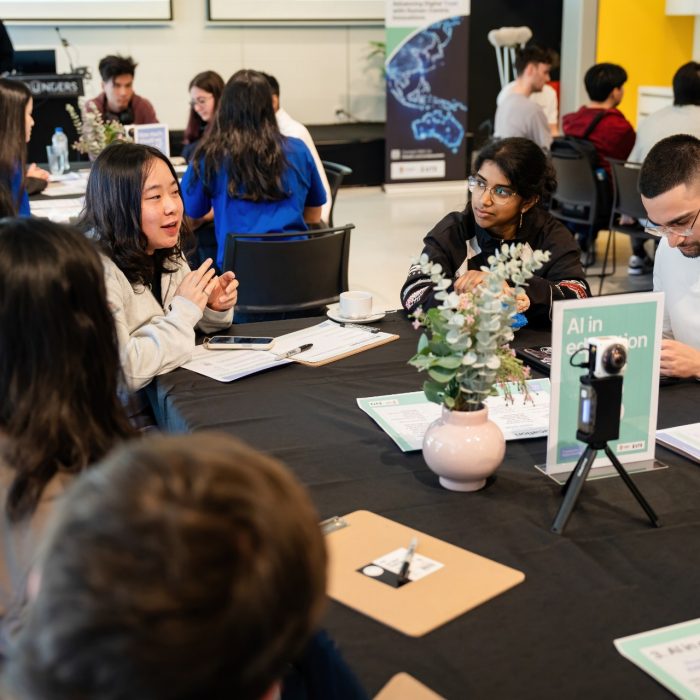 Participants discussing ideas around a table with worksheets and a small recording camera at the UNSW–UTS TDS Student Forum.