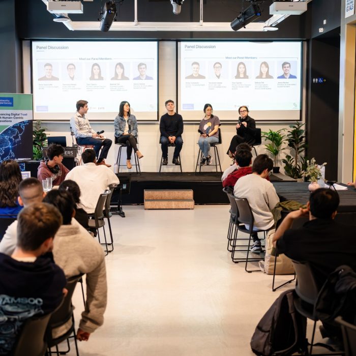 Wide view of an audience seated at tables facing five panellists at the UNSW–UTS TDS Student Forum.