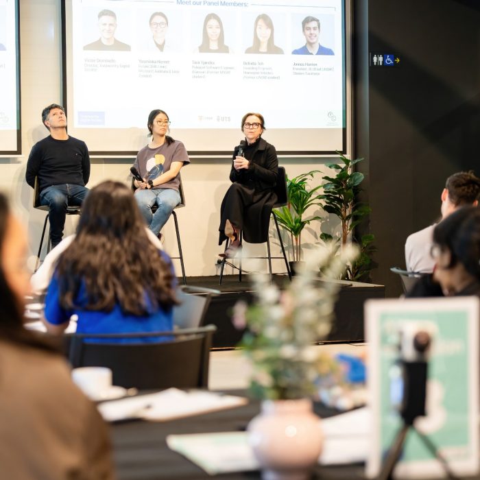 Audience members watching four panellists seated in front of presentation screens at the UNSW–UTS TDS Student Forum.