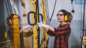 Portrait of apprentice engineering worker young woman working, examining and operating CNC plastic injection molding machinery in factory warehouse after studied manufacturing apprenticeship program certifies XXXL