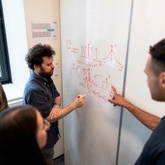 four Engineering students writing on and viewing whiteboard