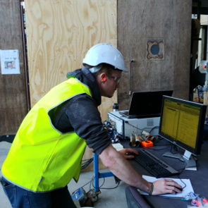 Flow noise rsearch, man with hard hat and high vis working on a computer outdoors at a job site