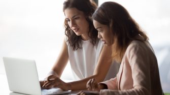 businesswomen workers talk discuss online project work together look at laptop in office, mentor teach intern, executive train employee using computer software