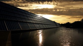 Solar panels over water, backlit by sunset
