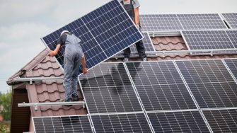 Workers mounting photovoltaic solar moduls on roof of house. Electricians in helmets installing solar panel system outdoors. Concept of alternative and renewable energy.