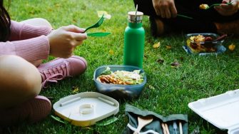 Students enjoying an outdoor picnic using reusable food containers, cups and a drink bottle on campus.