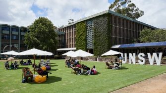 Students relaxing on the campus lawn beside the UNSW letters