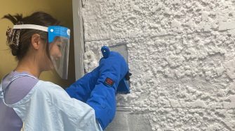Laboratory worker in a face shield spraying wall insulation