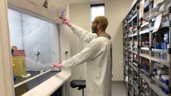 A scientist in a white lab coat operating a laboratory fume hood.
