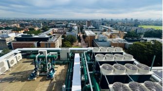 Rooftop air-conditioning and refrigeration units on a UNSW campus building, with the Sydney cityscape in the background.