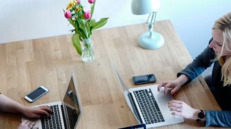 Two women working from home on laptops at dining table
