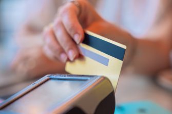 Close-up of a hand holding a credit card, performing a transaction on a contactless payment terminal. 