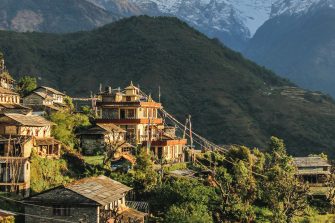 A landscape shot of Nepal shows homes on a hillside in the foreground and ice capped mountains in the distance.