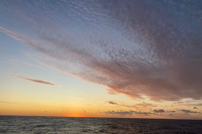 A photograph taken looking out at the horizon at sunset with clouds occupying part of ther sky, and the rest a clear late afternoon.