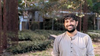 A photo of Gautum Bhatia standing and smiling at the camera in front of a fig tree 