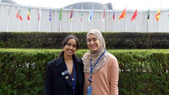 Photo of Rayana and Samar in front of the UN flags