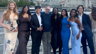 A group of seven people dressed in formal attire posing for a photo with the River Thames in the background.  