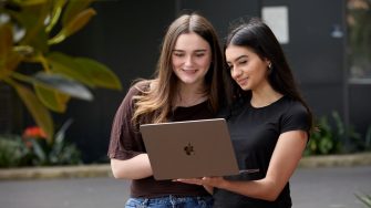 Two high school students holding a laptop together and reading the screen